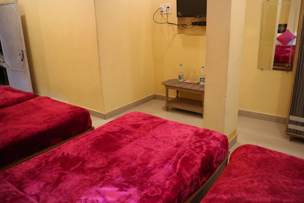 A hotel room with two beds covered in red bedding, a small wooden table with water bottles, and a television mounted on the wall.