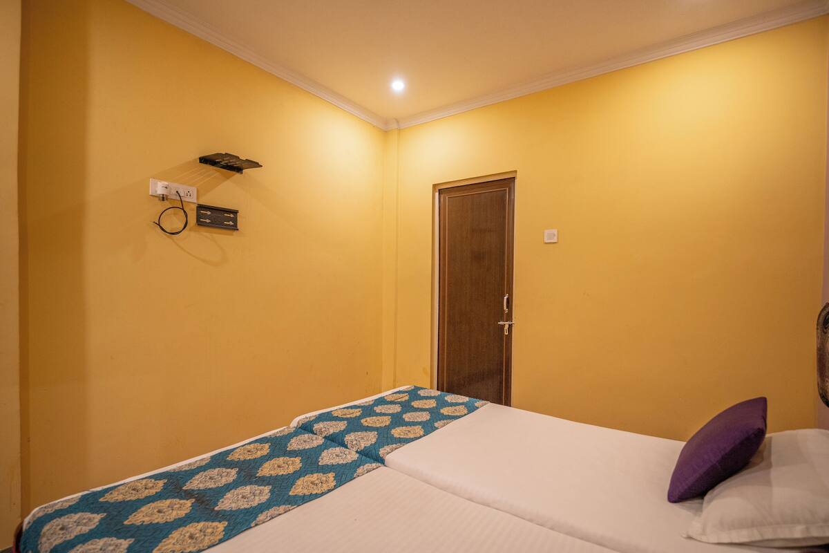 A hotel room with a bed, a bedside table, a wall socket, and a door.