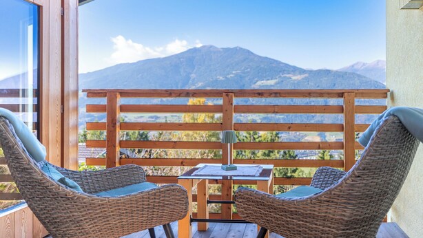 A wooden deck with wicker chairs and a table, overlooking a mountain range. - Haus Lasaun (Bressanone)