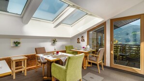 A dining area with a high ceiling and skylights, wooden furniture, and a view of a mountainous landscape through large glass doors. - Haus Lasaun (Bressanone)