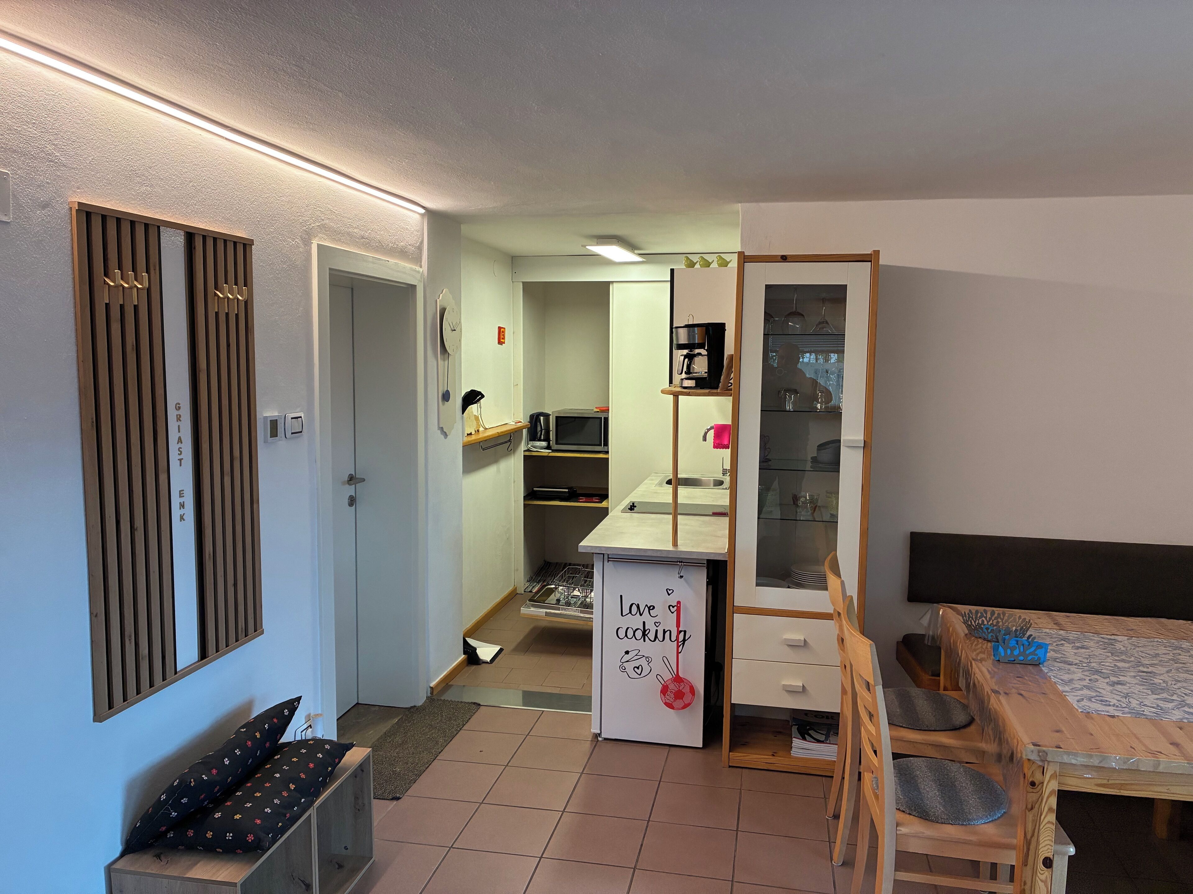 A compact kitchen with a microwave, coffee maker, and a small sink. There is a wooden cabinet with a clock and a sign that says "Love cooking".
