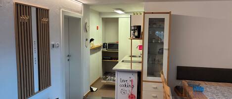 A compact kitchen with a microwave, coffee maker, and a small sink. There is a wooden cabinet with a clock and a sign that says "Love cooking".