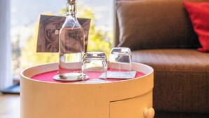 A round table with a bottle, glasses, and a card in a room with a sofa and a view of mountains. - Haus Lasaun (Bressanone)
