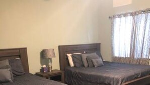 A bedroom with two wooden beds, a nightstand with a lamp, and a window with curtains. - Royal Retreat 3 Downtown South Charleston  (South Charleston)