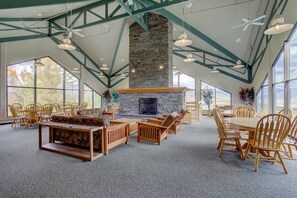 Una habitación amplia con chimenea de piedra, muebles de madera y ventanas grandes.