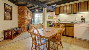 A dining area with a wooden table and chairs, a brick fireplace, and wooden cabinets in the kitchen. - Lively condo-central location! Ready your great adventures for every season! (Silverthorne)
