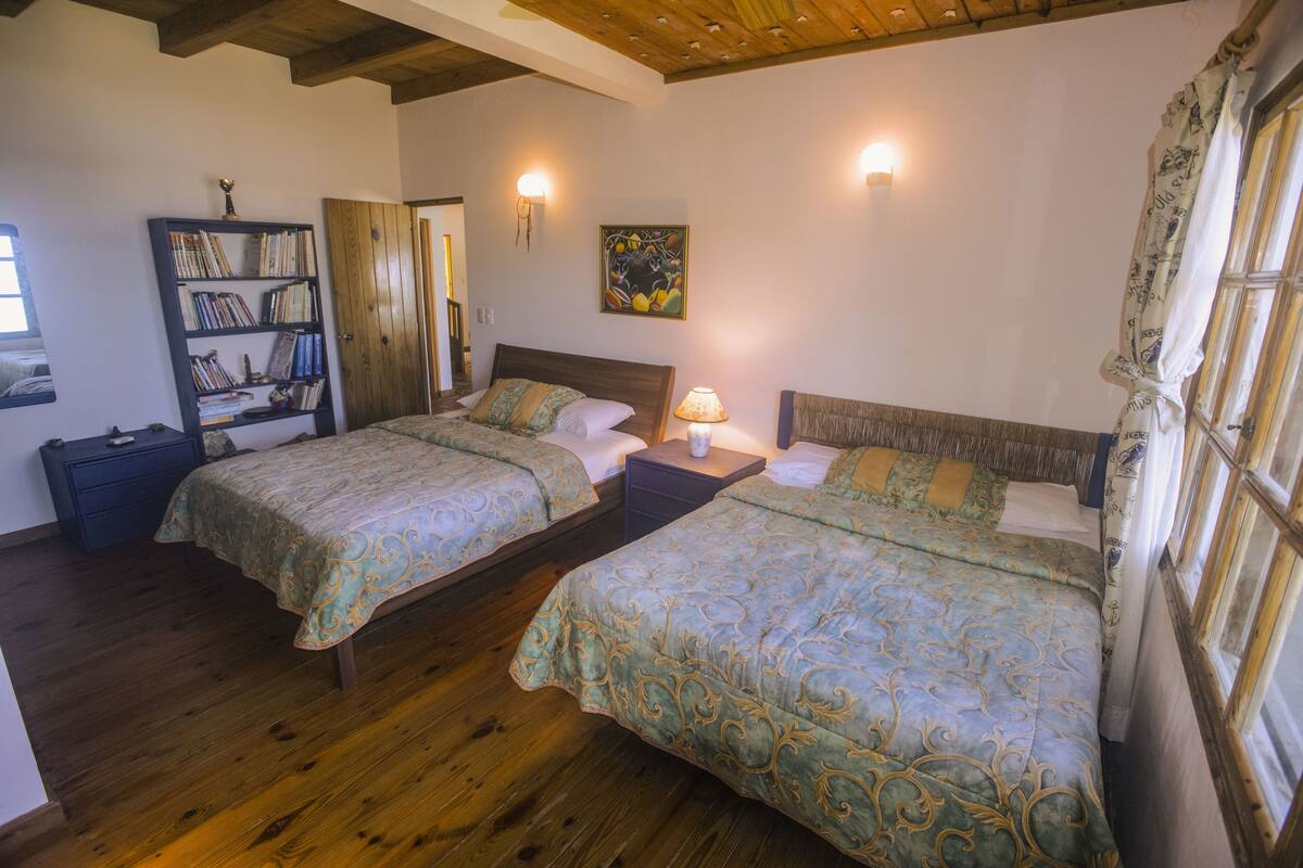 A bedroom with two beds, wooden flooring, a bookshelf, and a painting on the wall.