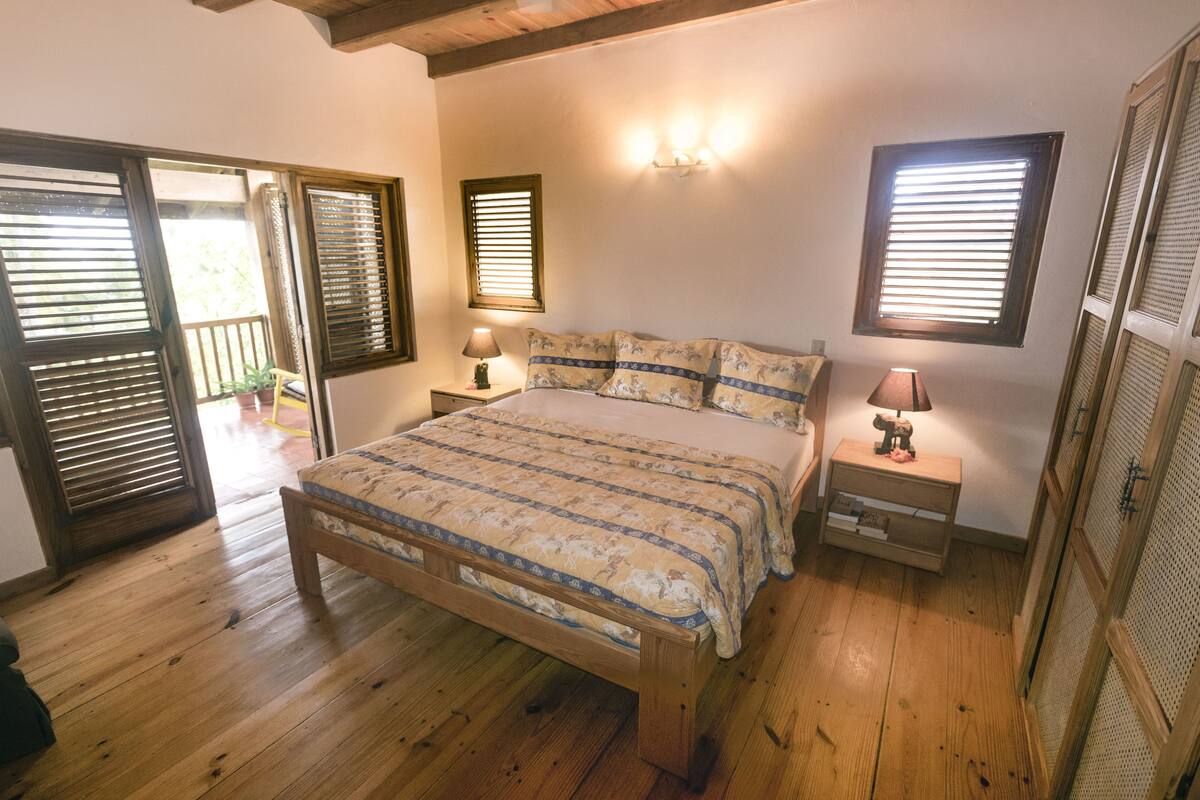 A bedroom with a wooden bed, two bedside tables with lamps, and a window with blinds.