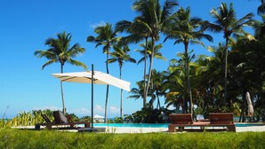 A poolside area with lounge chairs and umbrellas, surrounded by palm trees. - Villa Natasha (Las Galeras)