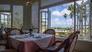 A dining area with a table set for two, overlooking a pool and palm trees. - Villa Natasha (Las Galeras)
