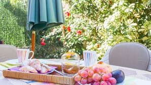 Une table dressée à l’extérieur, avec un panier de viennoiseries, une assiette de raisins et un bocal en verre.