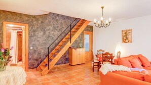 Un vaste espace de vie agrémenté d’un escalier en bois, d’une table à manger avec des chaises, d’un canapé et d’un lustre.