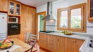 Une cuisine avec des meubles en bois, un four à micro-ondes, un four traditionnel, une cuisinière à gaz et une fenêtre donnant sur un paysage verdoyant.