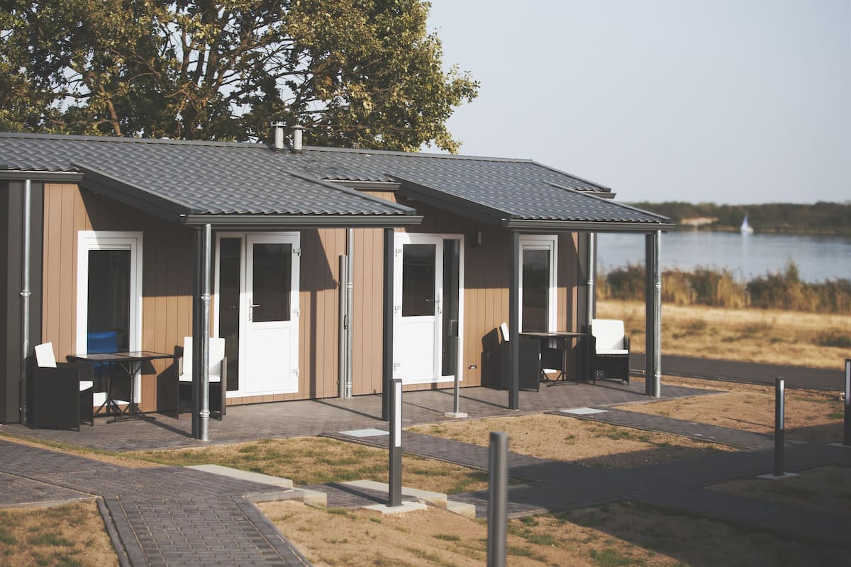 A modern outdoor building with a covered patio area, a table with chairs, and a view of a lake.