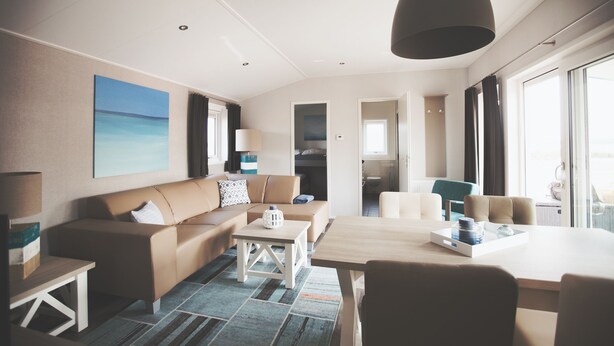A modern hotel room with a sofa, a dining table, and a large window.