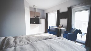 A hotel room with a bed, a desk, two chairs, a television, and a window with curtains.