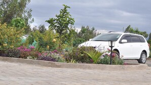 A white SUV parked in a landscaped area with a variety of plants and flowers. - Peaks Hotel Limited (Nanyuki)