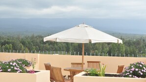 A terrace with a table and chairs, an umbrella, and a view of a forested landscape. - Peaks Hotel Limited (Nanyuki)