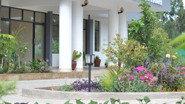 A hotel with a modern facade, large windows, and a covered entrance area with potted plants and flowers. - Peaks Hotel Limited (Nanyuki)
