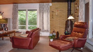 Una sala de estar acogedora con sillones de cuero, chimenea, estantería y un ventanal con cortinas.