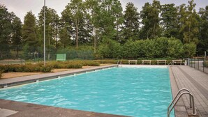 Una piscina rectangular con agua cristalina azul, rodeada por una terraza pavimentada y una cerca de metal.