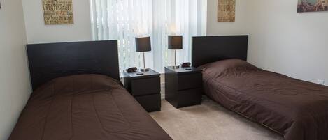 Un dormitorio con dos camas individuales, un espejo, mesitas de noche y una cortina decorativa.