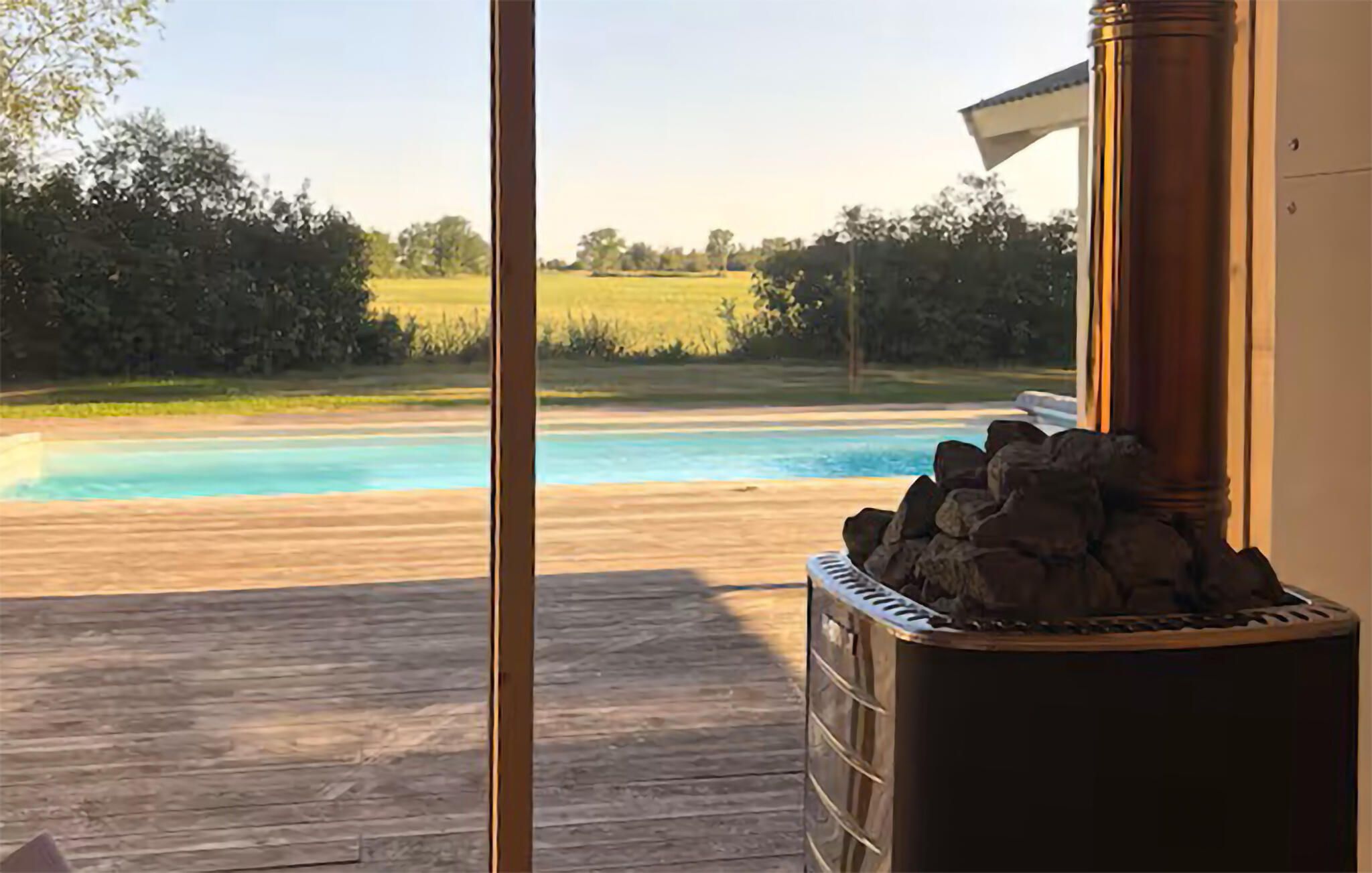 Une piscine avec une terrasse en bois et un élément décoratif en pierre, vraisemblablement une cheminée, au premier plan.