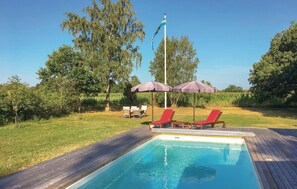 A swimming pool with a wooden deck, two red lounge chairs, and a flagpole with a flag.