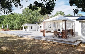 A covered outdoor seating area with wooden chairs and a table, surrounded by a white building with a porch. - Awesome home in Löttorp with sauna (Löttorp)