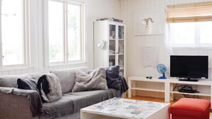 A living room with a grey sofa, a coffee table with a floral pattern, a television, a cabinet with books, and a window with blinds. - Awesome home in Löttorp with sauna (Löttorp)