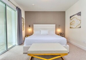 A modern bedroom with a large bed, bedside lamps, a bedside table, and a view through a glass door. - Aco258634 - The Encore Club Resort - 10 Bed 10 Baths Villa (Kissimmee)