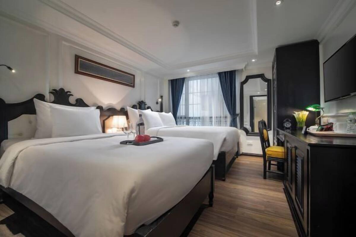 Une chambre d’hôtel avec deux lits, un bureau, une télévision et une fenêtre avec des rideaux.