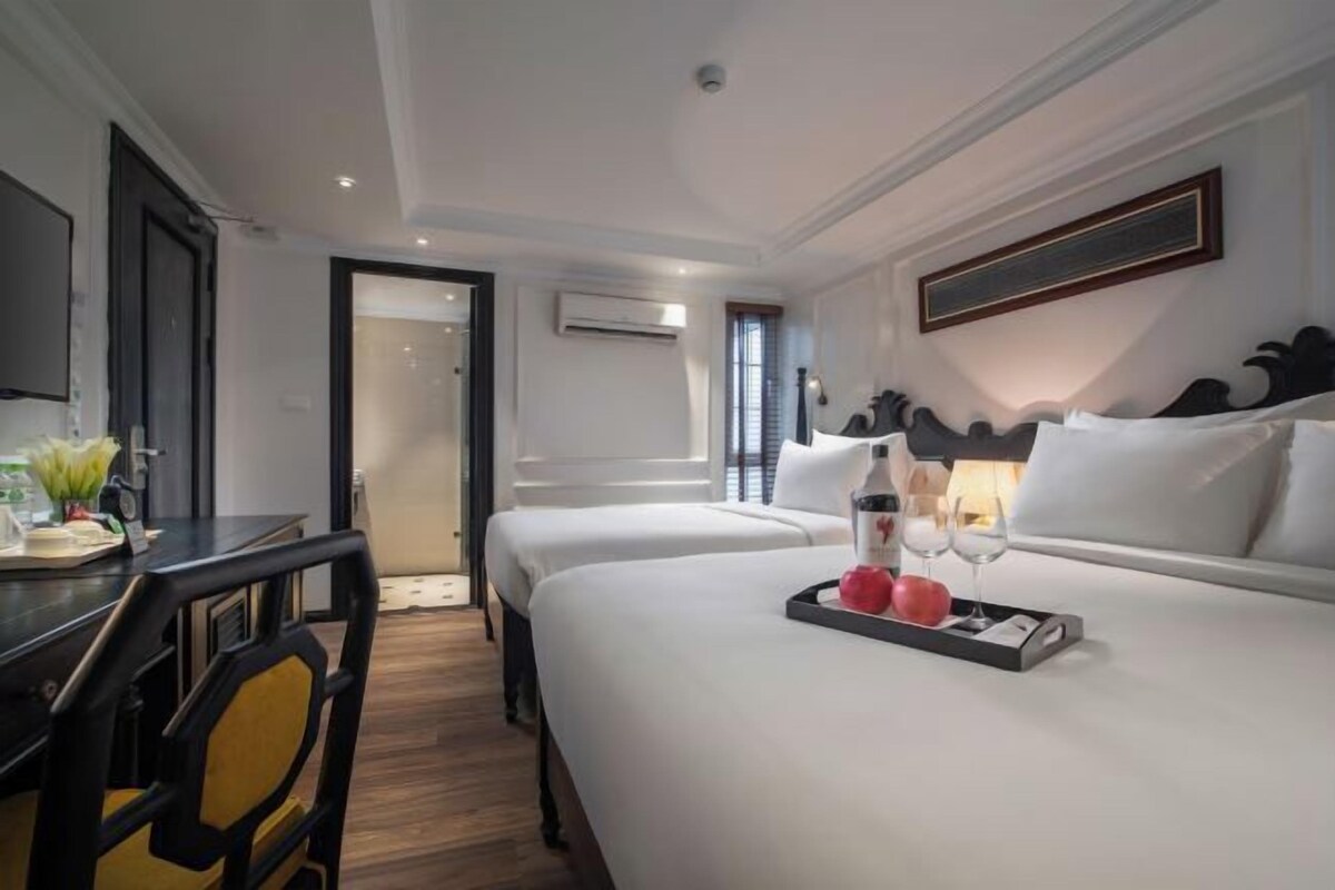 Ein Hotelzimmer mit zwei Betten, einem Schreibtisch mit Stuhl, einem kleinen Tisch mit Tablett und einem gerahmten Bild an der Wand.