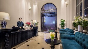 A hotel lobby with a reception desk, a receptionist, a seating area with sofas, and a large arched doorway leading outside. - My Boutique Hotel & Spa (Sa Pa)