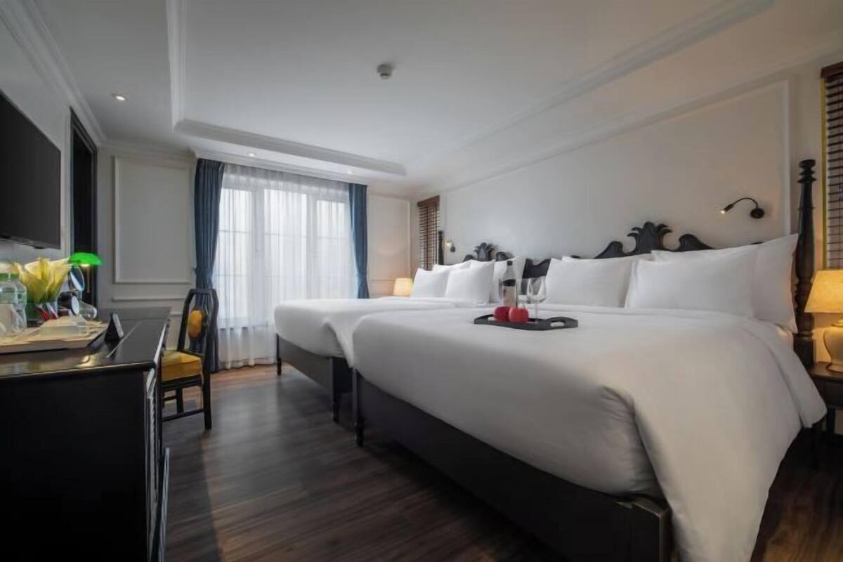 Une chambre d’hôtel avec un grand lit, un bureau avec une chaise, une télévision et une fenêtre avec des rideaux.