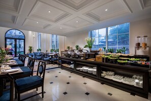 A hotel dining area with a buffet, seating arrangements, and large windows. - My Boutique Hotel & Spa (Sa Pa)