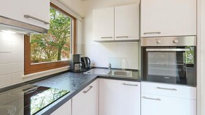 A modern kitchen with white cabinets, a built-in oven, a coffee maker, and a window with a view of trees.