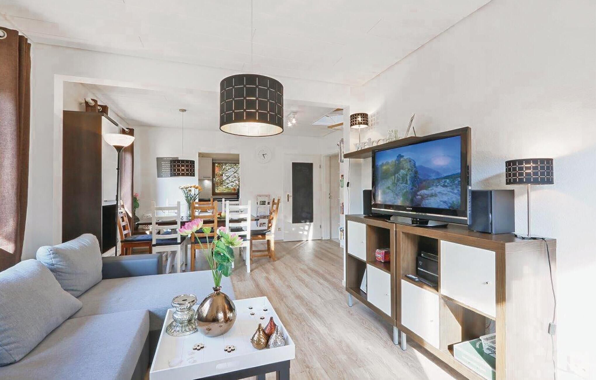 A modern living room with a sofa, a coffee table with decorative items, a flat-screen TV on a wooden stand, and a dining area in the background.