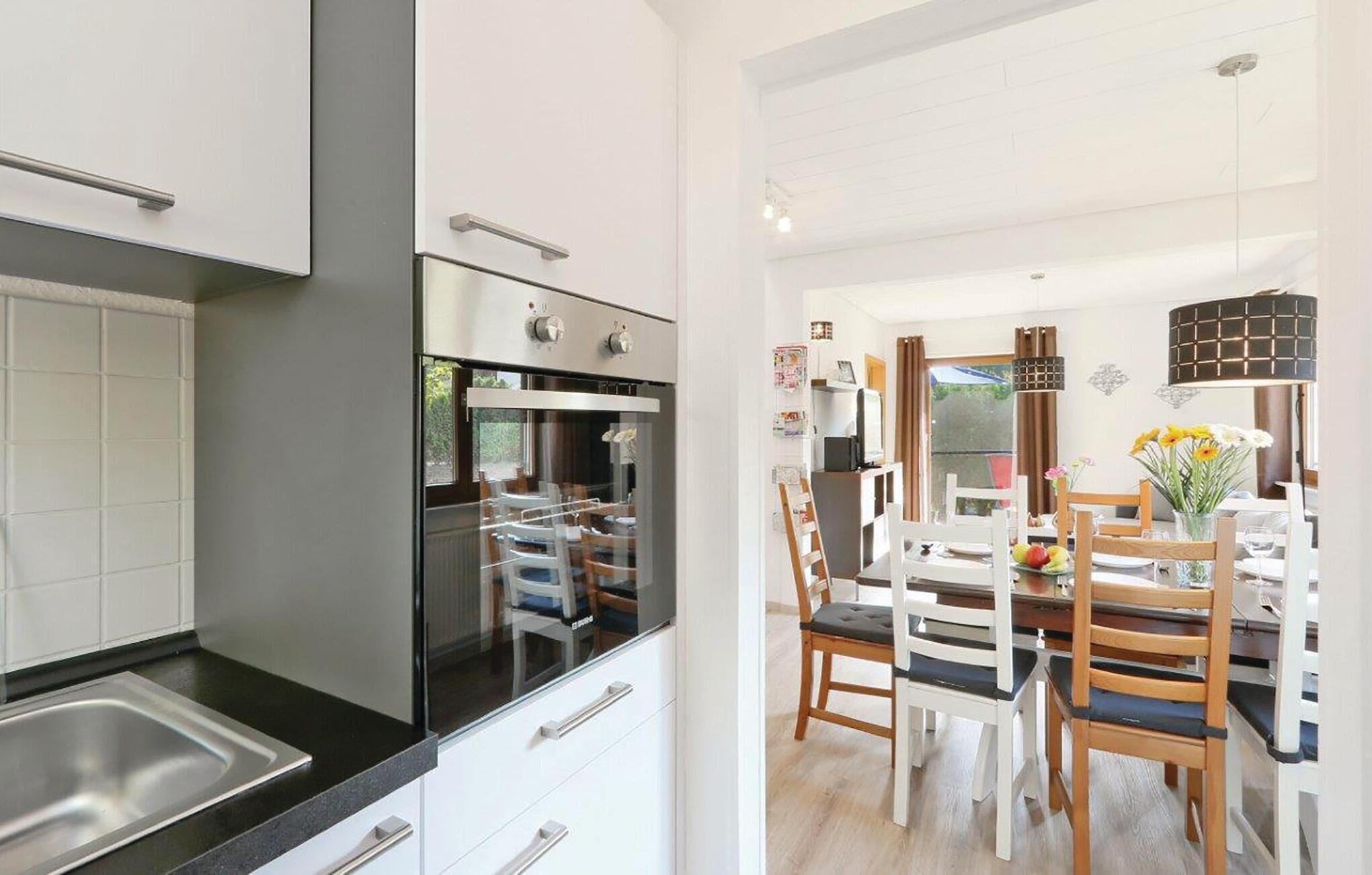 Eine moderne Küche mit Edelstahlgeräten, ein Essbereich mit Holztischen und -stühlen sowie ein Blick ins Freie durch ein Fenster.