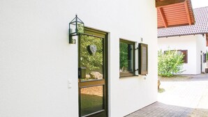 A white building with a black door, a window with shutters, and a small outdoor area with a paved path.
