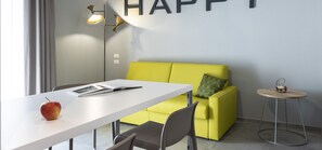 A modern room with a white desk, a yellow sofa, a small round table, and a wall-mounted lamp. - Marconi 1935 B&B and Holiday Home (Follonica)