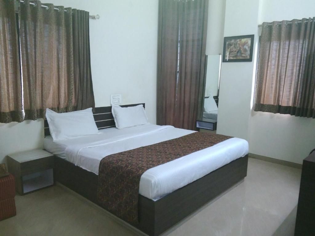 A hotel room with a single bed, a nightstand, a bedside table, and a mirror.