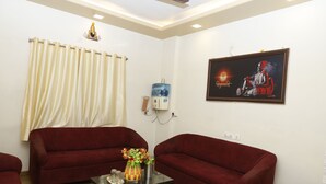 A room with two red sofas, a glass coffee table with decorative items, a water dispenser, and a framed picture on the wall. - Balaji Lodging (Pandharpur)