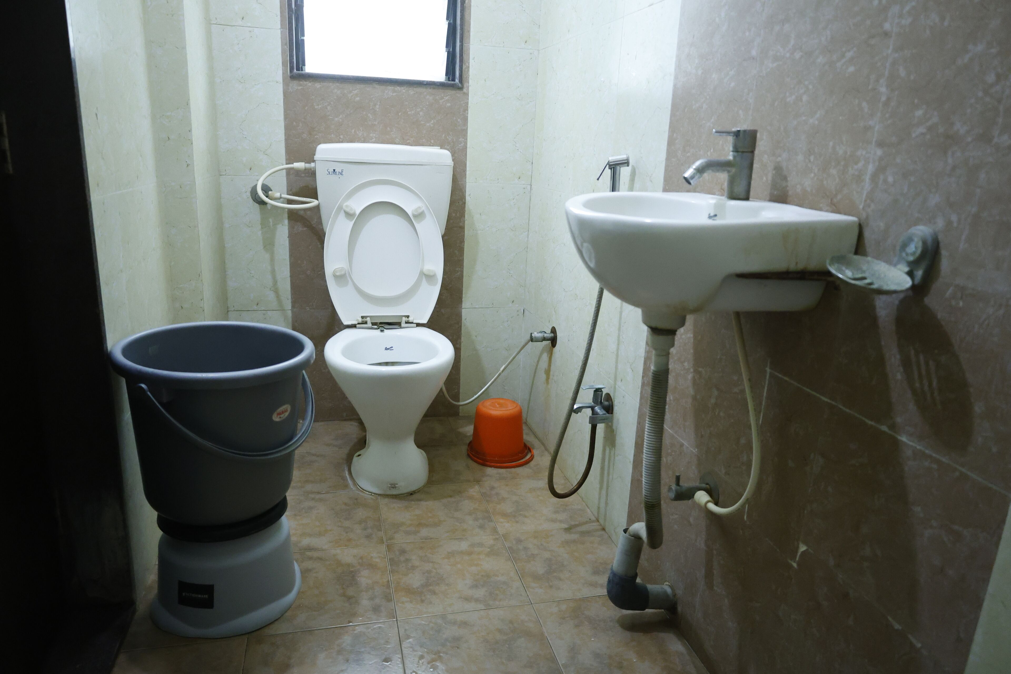A small bathroom with a toilet, sink, and bucket.