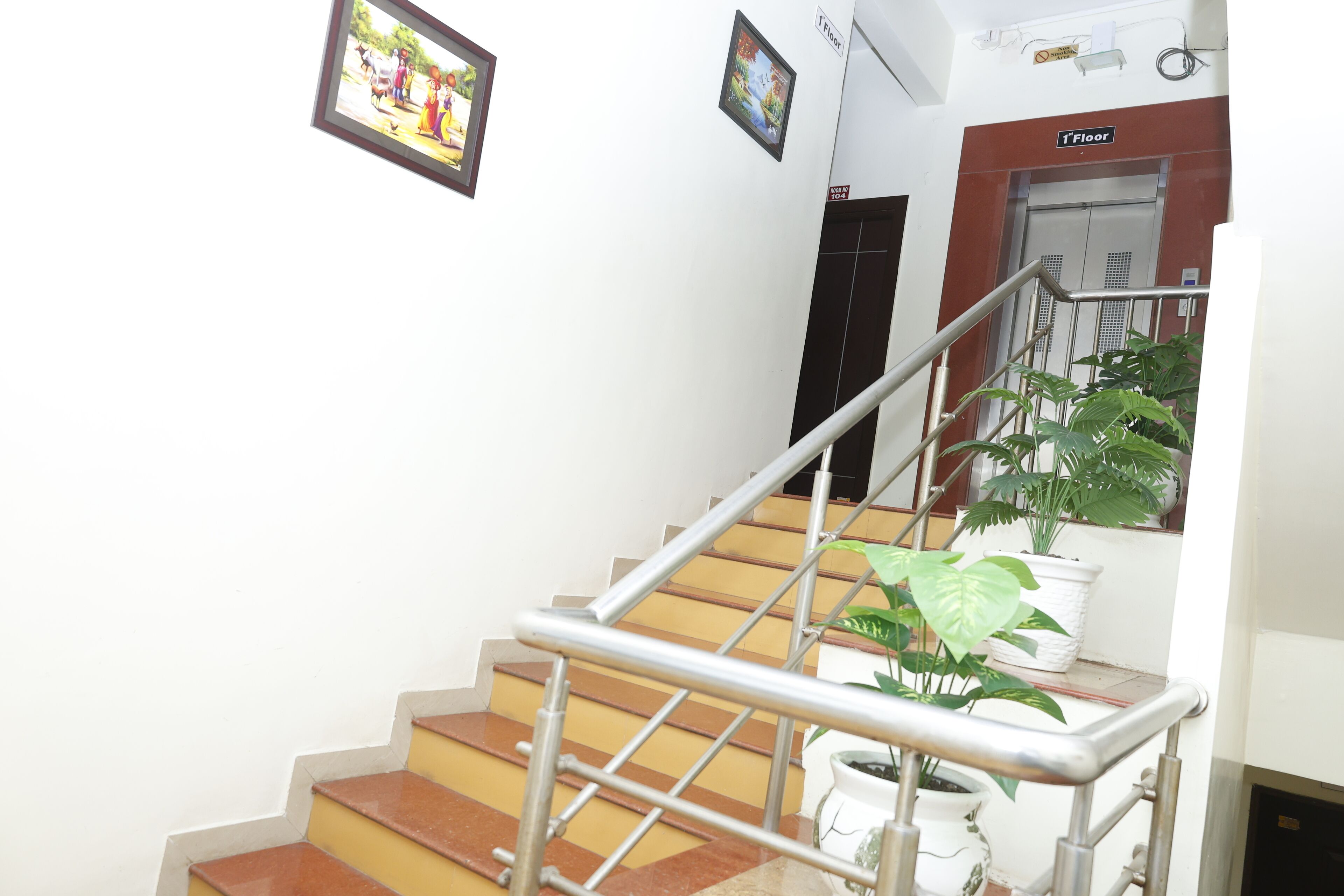 Una escalera con barandillas metálicas, una planta en maceta y una puerta con el letrero '1er Piso'.