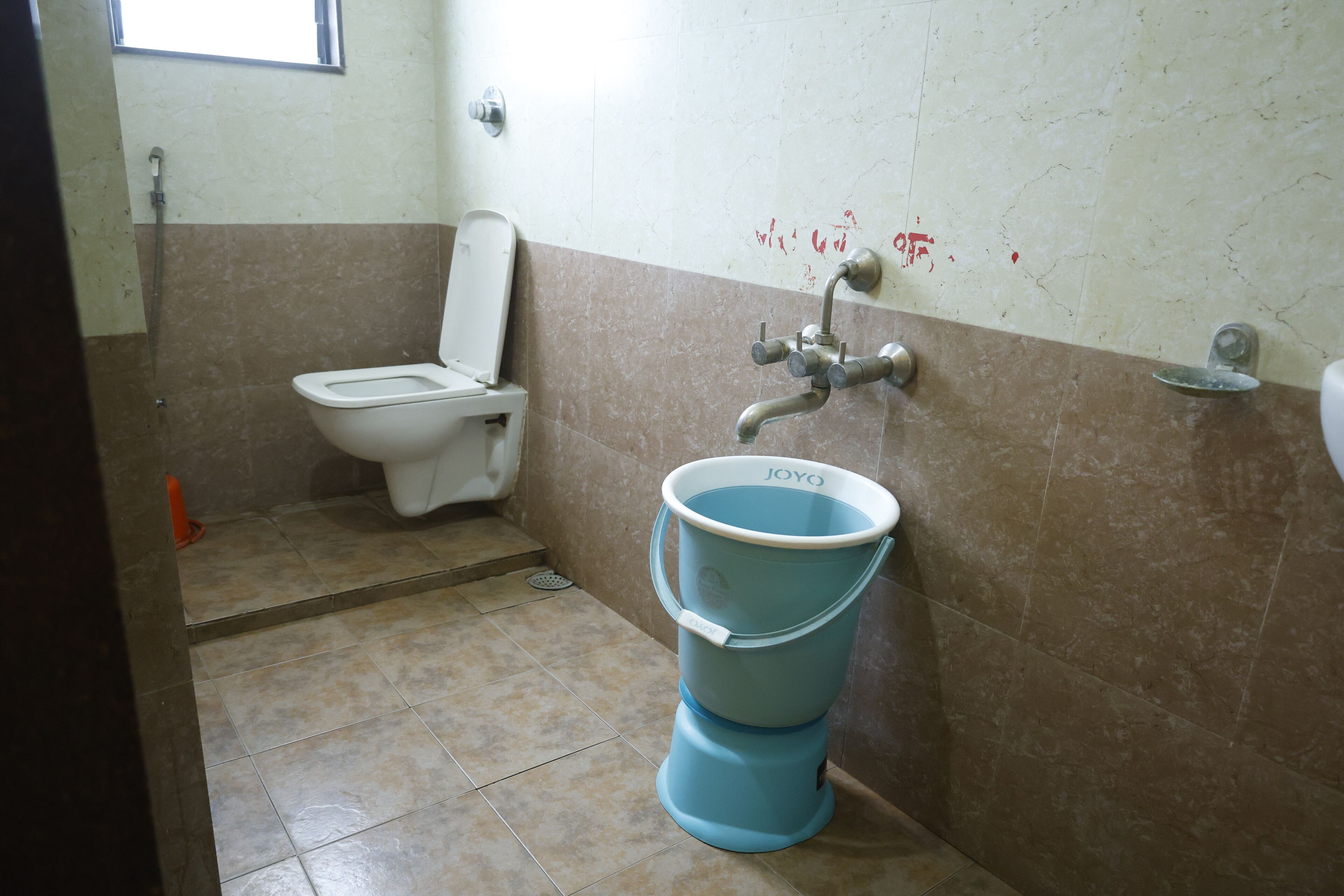 Un baño con inodoro, un cubo azul y ducha.