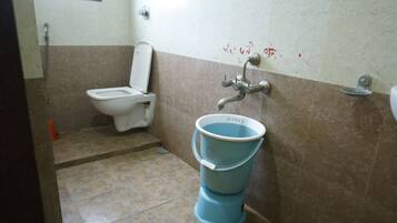 Un baño con inodoro, un cubo azul y ducha.
