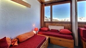 A cozy room with a wooden ceiling, a window with a mountain view, and a bed with red bedding.