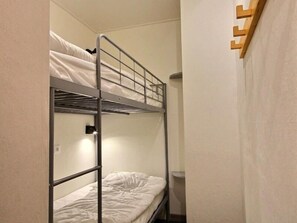 Ett rum med en våningssäng, ett litet nattduksbord och en hylla som är monterad på väggen.