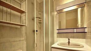 Een badkamer met een glazen douchecabine, een wastafel met een spiegel erboven en een toilet met een papieren handdoekdispenser.